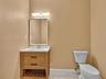 Wood-finish vanity with a rectangular sink, white countertop, matte black hardware, and an integrated slatted lower shelf, paired with a modern framed
