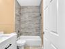 Bathroom featuring a white vanity cabinet with a stone-surface countertop, tub-shower combination with full-height neutral-toned tile surround, built-