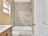 Bathroom featuring a tub-shower combination with floor-to-ceiling stone-look tile surround, built-in wall niche, wood-finish vanity with a rectangular