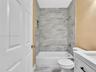 Full-height gray veined tile shower surround with integrated storage niche, white acrylic soaking tub, vanity with clean-lined cabinetry, and hardware