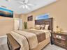 Neutral-toned bedroom featuring tile flooring, horizontal window with integrated blinds, and a ceiling-mounted light fixture with a fan