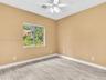Neutral-toned interior space featuring wood-finish tile flooring, a multi-blade ceiling fan with integrated lighting, and a single-pane window