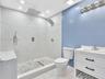 Walk-in shower featuring large-format tile walls, a pebble-stone floor, and a rainfall showerhead, complemented by a white vanity with integrated basi