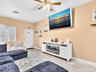 Neutral-toned interior space featuring wood-finish flooring, a ceiling fan with integrated lighting, and a white built-in media console with an electr