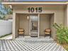 Covered entryway featuring a concrete stoop, geometric permeable paver driveway, wall-mounted exterior lighting, and stucco-style facade