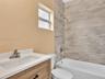 Vanity featuring a light wood-finish cabinet, white solid-surface countertop, and integrated sink, complemented by a tub-shower combination with large