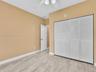 Neutral-toned interior featuring wood-finish flooring, a white six-panel door, floor-to-ceiling louvered-style closet doors, and a ceiling-mounted lig