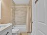 Bathroom featuring neutral-toned wall tile surround, white porcelain bathtub, vanity with integrated basin, and shaker-style cabinetry