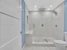 Walk-in shower featuring floor-to-ceiling stone-finish tile, a built-in stone bench, a recessed wall niche, a rain-style showerhead with handheld spra