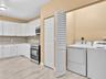 Kitchen featuring white cabinetry, stone-finish countertops, stainless steel appliances, wood-finish tile flooring, and a dedicated laundry area with 