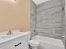 White vanity with a rectangular sink, matte black hardware, tiled shower surround with a built-in recessed niche, and polished metal fixtures