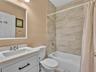 Bathroom featuring a white vanity with a rectangular basin, stone-finish countertop, frameless mirror, and shower-tub combination with horizontal wall