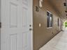 Exterior entrance featuring a six-panel white door, smooth stucco finish, wall-mounted light fixture, and concrete walkway