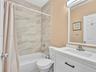 Bathroom featuring a white vanity with an integrated basin, neutral tile-surround tub, modern brushed-nickel fixtures, and a framed mirror with integr