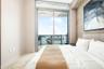 Floor-to-ceiling sliding glass door, exposed concrete structural beam, textured accent wall, and private balcony with railing