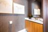 Textured wall covering, wood-finish vanity cabinet, light-toned countertop with an integrated rectangular sink, wall-mounted mirror, and chrome-finish