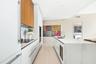 Kitchen featuring white flat-panel cabinetry, wood-finish upper cabinets, stone-surfaced waterfall island, built-in wall oven, and integrated wine coo