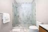 Walk-in shower featuring a frameless glass enclosure, floor-to-ceiling stone-finish wall tiles, and a wall-mounted shower head