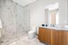 Bathroom featuring a walk-in shower with frameless glass enclosure, floor-to-ceiling stone-pattern tile, wood-finish cabinetry, white countertop, and 
