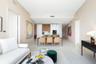 Open-concept interior featuring light-toned flooring, high ceilings, custom wood and white cabinetry, a built-in oven, and a kitchen island with stone