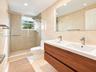 Double vanity with a wood-finish cabinet and integrated dual sinks, walk-in shower featuring glass doors and mosaic tile accents, wall-to-wall mirror,