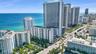 High-rise coastal property featuring white concrete exterior architecture, private balcony tiers, expansive ocean frontage, and manicured palm landsca