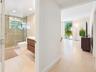 Bathroom featuring a wood-finish floating vanity, glass-enclosed shower with tiled walls, and large-format tile flooring extending into the living are