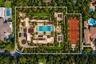 Aerial perspective of a sprawling estate featuring a clay tennis court, large swimming pool with built-in spa, expansive manicured grounds, covered pa