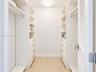 Walk-in storage space featuring built-in white cabinetry, multi-tiered adjustable shelving, integrated drawers with metallic pulls, and wood-finish fl