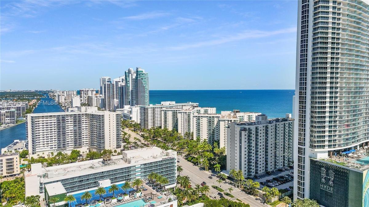 High-rise cityscape featuring multi-story residential structures, coastal proximity, prominent ocean water, and established palm tree landscaping