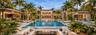 Custom swimming pool with stone decking, integrated fire pit with perimeter seating, covered outdoor structures, and mature palm landscaping