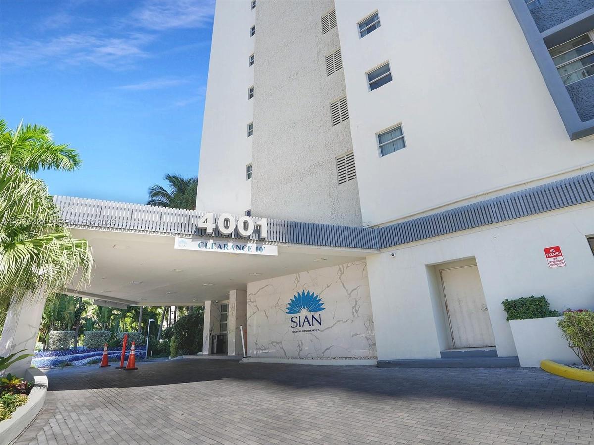 High-rise building exterior featuring a covered porte-cochère, paved driveway, stone-clad accent wall, and decorative metal detailing