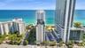 Aerial perspective of a multi-structure beachfront complex featuring high-rise architecture, paved surface parking, and direct access to the coastline