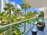 Covered balcony featuring glass railing panels and metal handrails, framed by mature palm trees