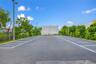 Asphalt parking area featuring marked spaces, perimeter chain-link fencing, mature trees, and installed exterior lighting poles