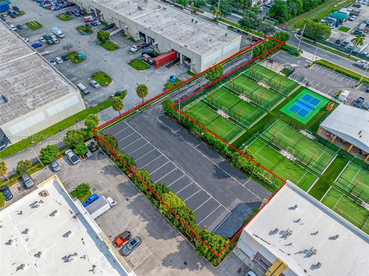 Asphalt-paved parking area featuring striped individual spaces, mature perimeter landscaping, and fenced boundaries