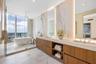 Bathroom featuring floor-to-ceiling stone wall cladding, a floating wood-finish dual vanity with integrated countertop basins, a deep soaking tub, and