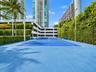 Hard-court tennis facility featuring blue acrylic surfacing, black perimeter chain-link fencing, integrated pole-mounted lighting, and extensive perim