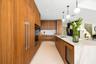 Modern kitchen featuring floor-to-ceiling wood-finish cabinetry, a waterfall-edge stone island, an integrated wine chiller, built-in wall oven, and pe