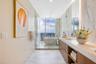 Floating vanity with wood-finish cabinetry, solid-surface countertop, full-height stone-finish wall cladding, and a freestanding soaking tub enclosed 