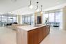 Kitchen island featuring a waterfall stone countertop, wood-finish cabinetry, an undermount sink, and polished metal faucet