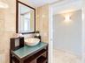 Bathroom featuring stone wall and floor tile, a dark wood-finish vanity with a glass countertop, a stone vessel sink, and a rectangular wall mirror wi