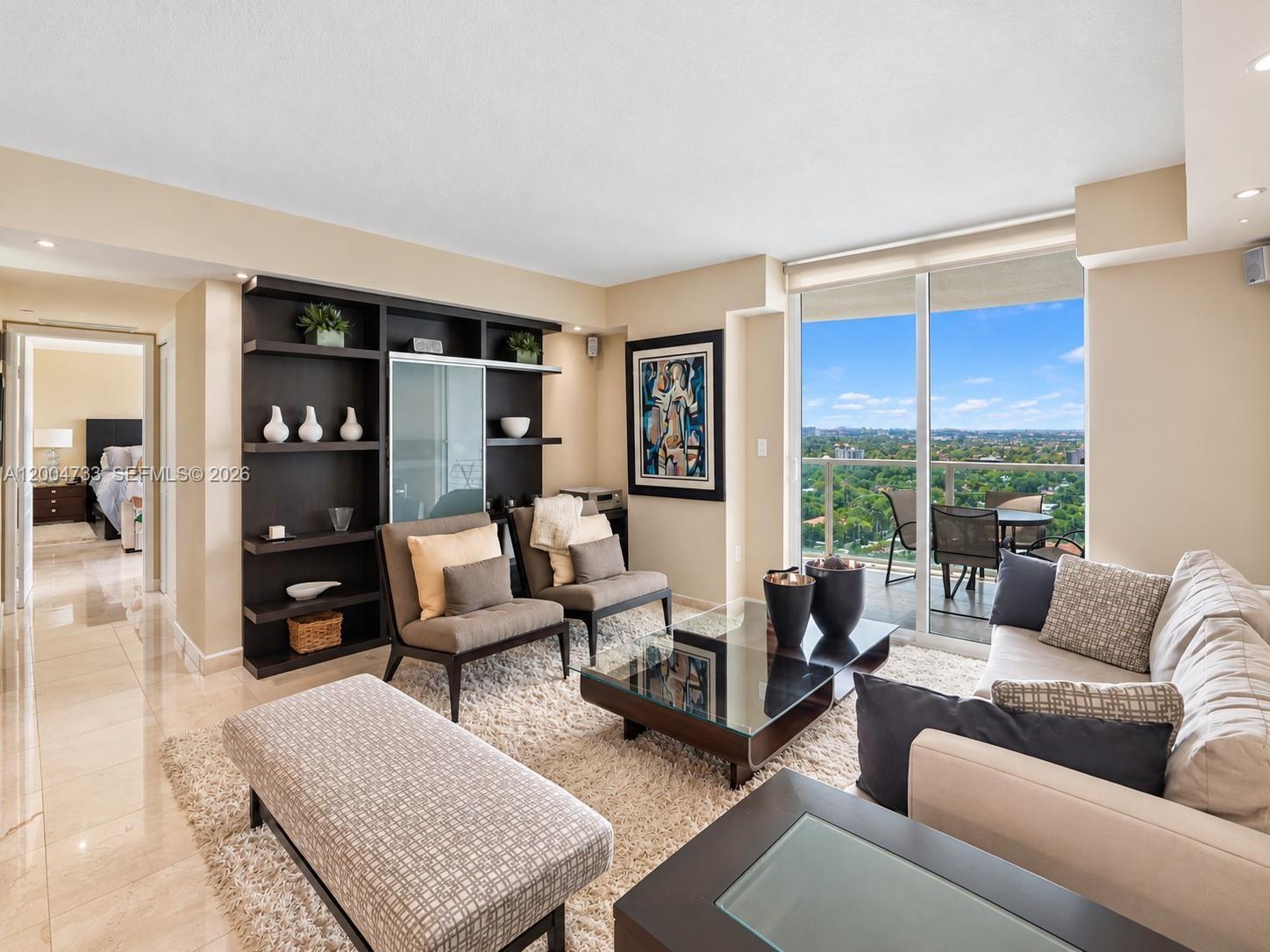 Living area featuring polished stone flooring, custom dark-finished built-in shelving, floor-to-ceiling glass sliding doors, and a private balcony