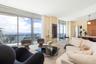 Floor-to-ceiling glass windows, expansive private balcony with glass railing, open-concept living area, custom flat-panel wood cabinetry, and neutral 
