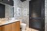 Floating wood-finish vanity with an integrated sink, large-scale wall mirror, patterned wall treatment, and black louvered door