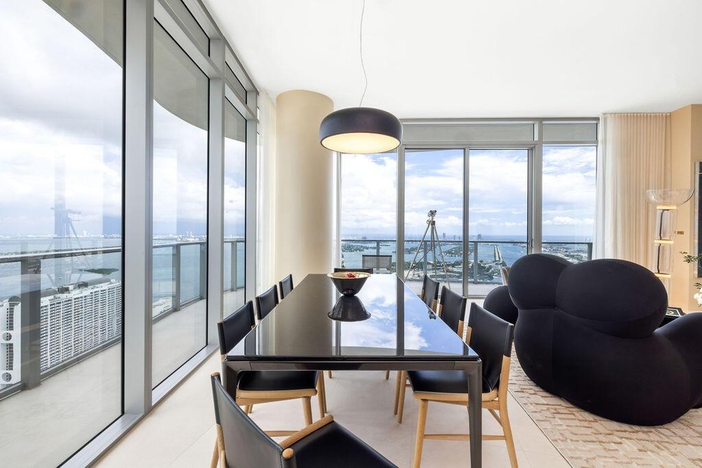 Floor-to-ceiling glass walls, wrap-around balcony with glass railing, cylindrical structural column, and modern pendant lighting
