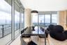 Floor-to-ceiling glass walls, wrap-around balcony with glass railing, cylindrical structural column, and modern pendant lighting