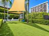Outdoor recreational space featuring synthetic turf, perimeter privacy hedging, mature palm trees, and overhead shade sails
