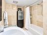 Full-height stone wall tiling, built-in floor-to-ceiling cabinetry with frosted glass panels, a white acrylic soaking tub, and a wall-mounted shower f