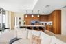 Modern kitchen featuring flat-panel wood cabinetry, a waterfall-edge kitchen island, stone backsplash, built-in wall oven, and three globe pendant lig